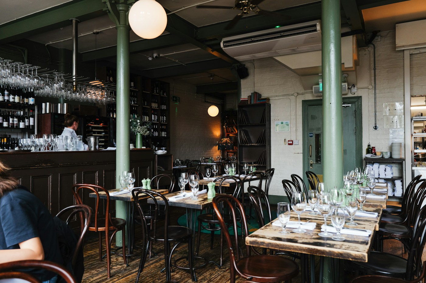 Warm restaurant dining room with rustic tables, bentwood chairs, pendant lights, and bar